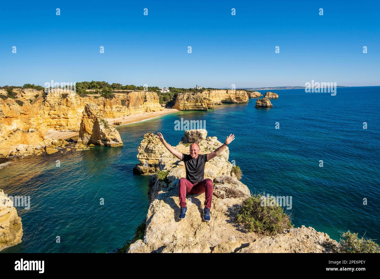Happy man sitting with hands up on the top of cliffs at Marinha beach, Algarve, Portugal Stock Photo