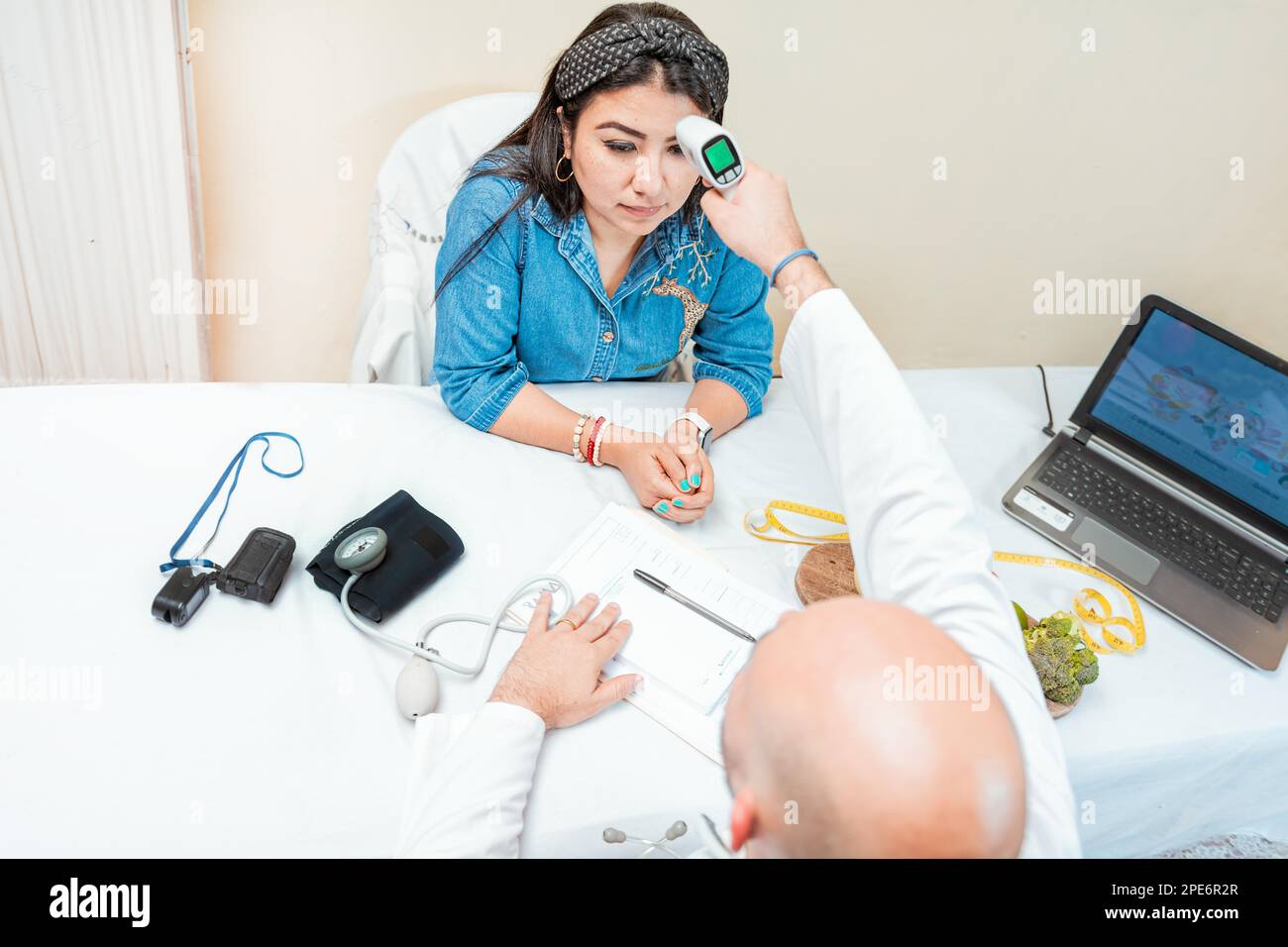 Male doctor taking temperature with gun to patient. Doctor measuring temperature with infrared gun to female patient, Doctor taking temperature to Stock Photo