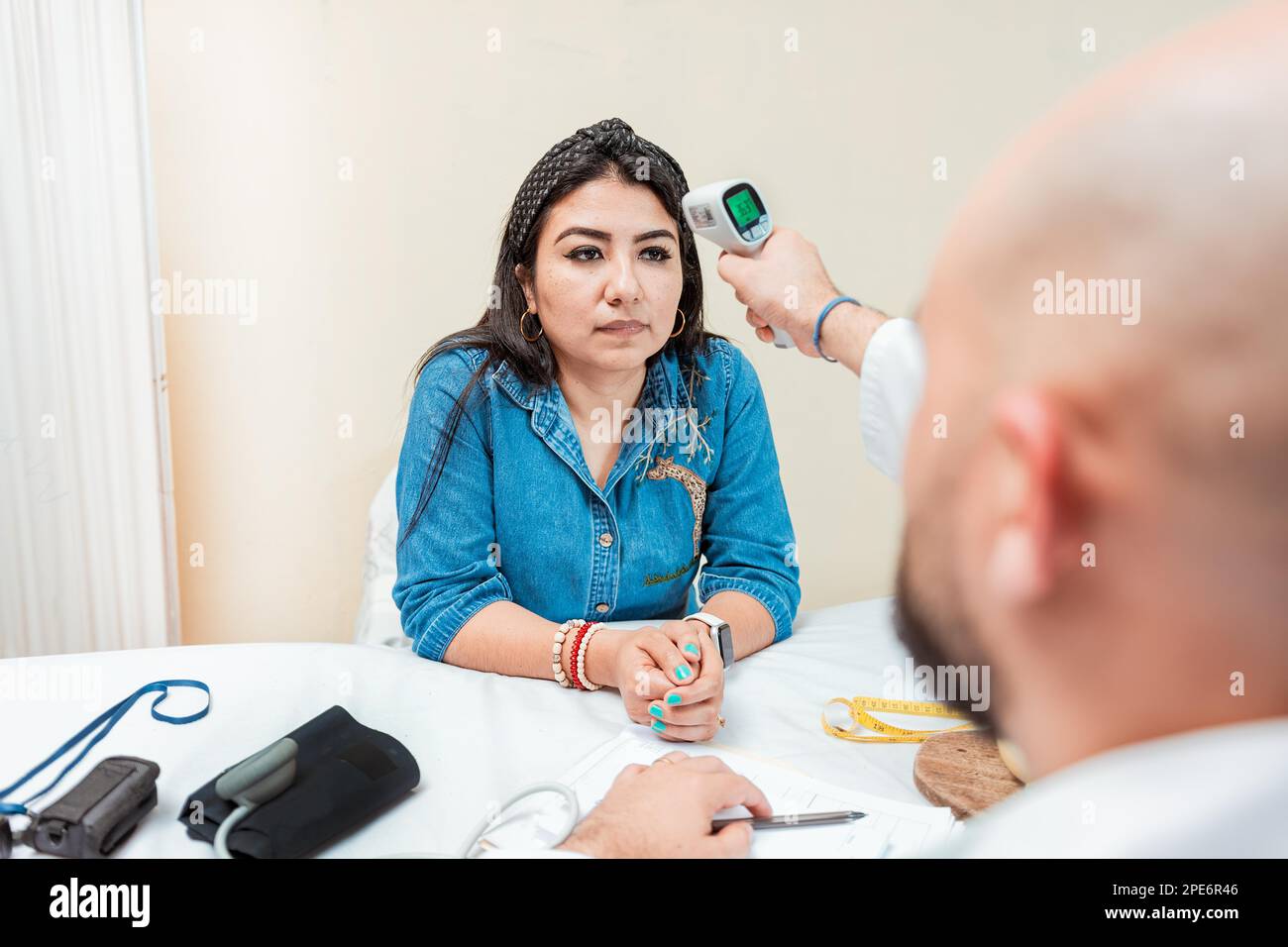 Doctor taking temperature to woman patient in office. Male doctor taking temperature with gun to patient. Doctor measuring temperature with infrared Stock Photo