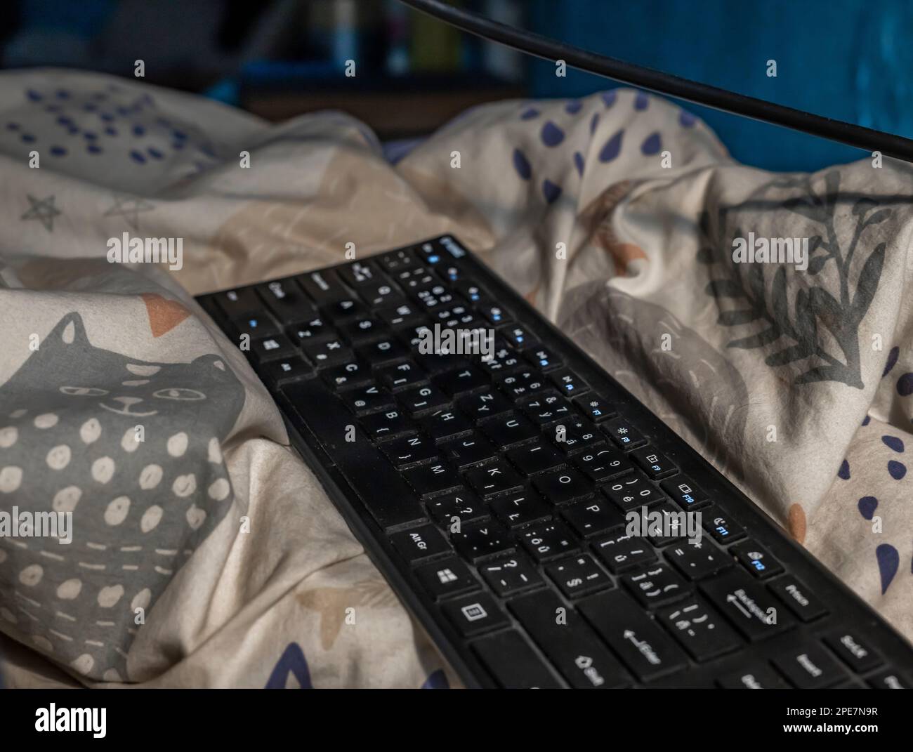Black keyboard in white bed linen with cats in dark interior Stock