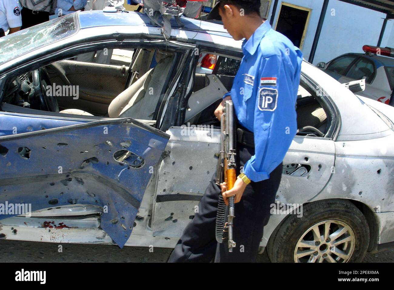 An Iraq Police officer looks over a damaged police car after a roadside ...