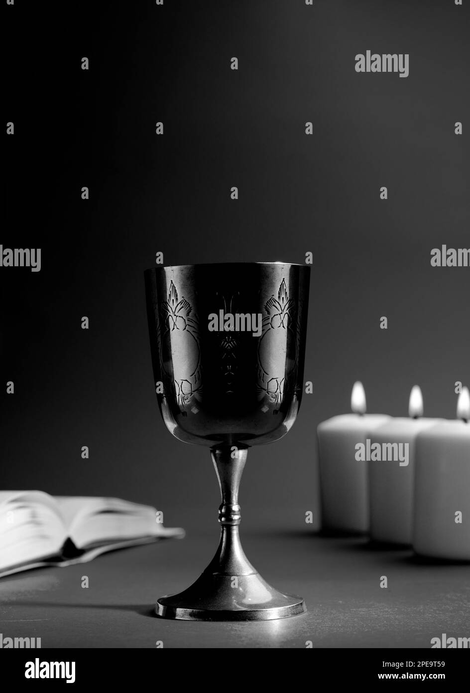 christian chalice with open bible and candles in the background. black