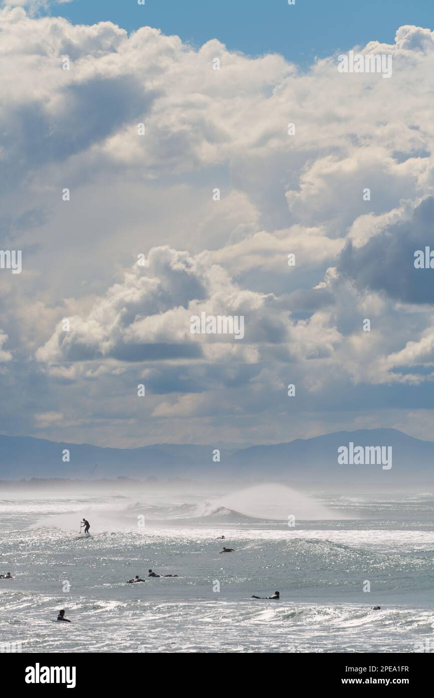 People surfing waves in Pegasus Bay New Zealand, with Kaikoura in the distance. Stock Photo