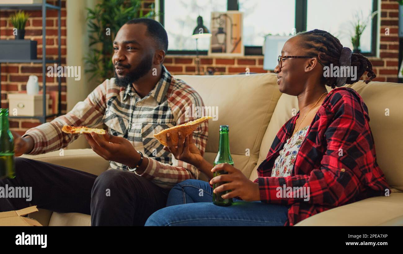 African american people eating slices of pizza in front of tv, binge