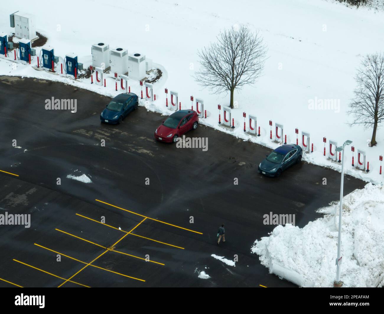 A high aerial photo looking at three parked Tesla electric vehicles at a Tesla Supercharger station in the winter. Stock Photo