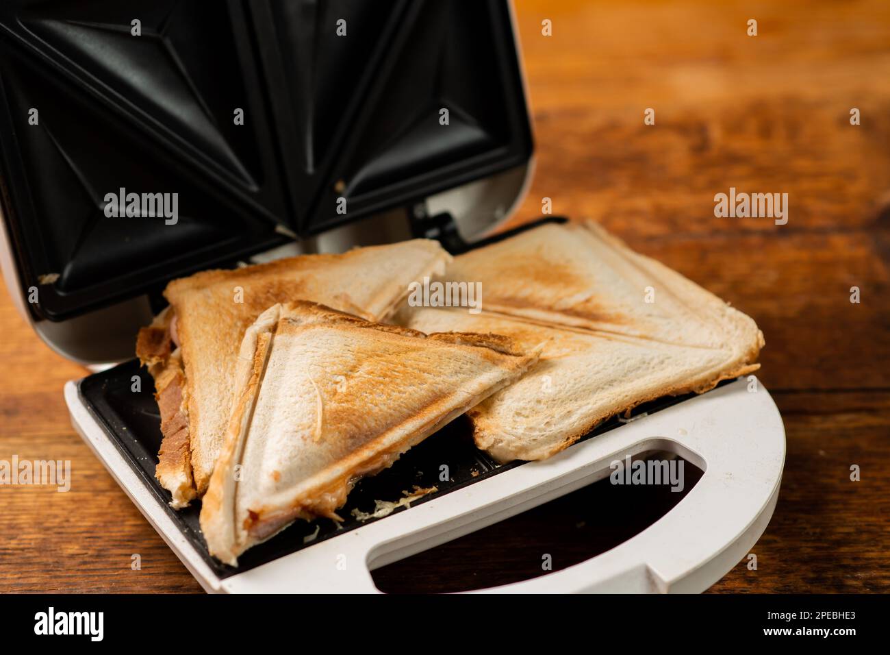 https://c8.alamy.com/comp/2PEBHE3/freshly-made-toasted-sandwiches-in-a-sandwich-maker-on-a-wooden-background-toasted-triangular-sandwiches-with-cheese-2PEBHE3.jpg