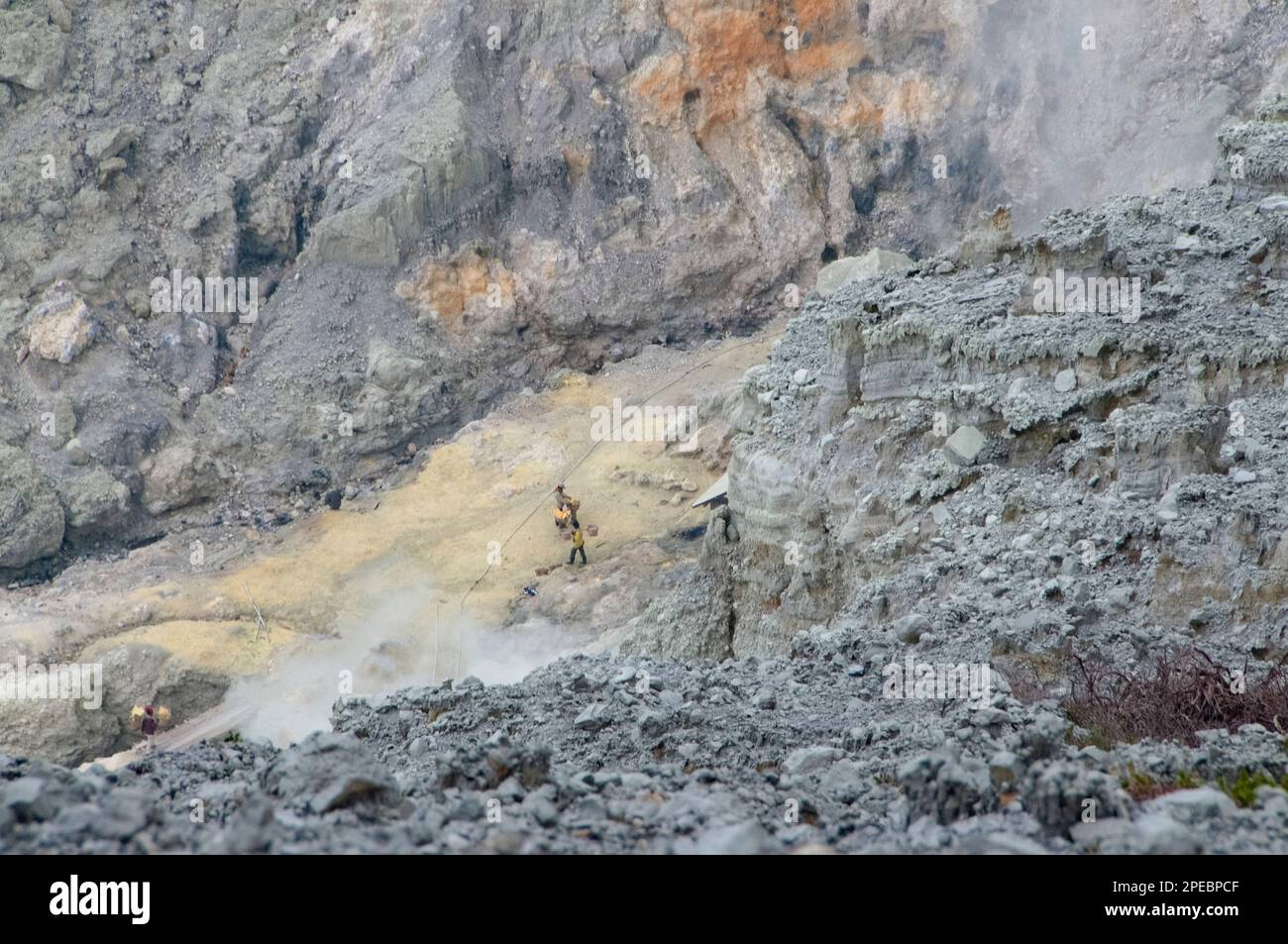 Local men carrying blocks of sulphur in baskets from centre of crater ...
