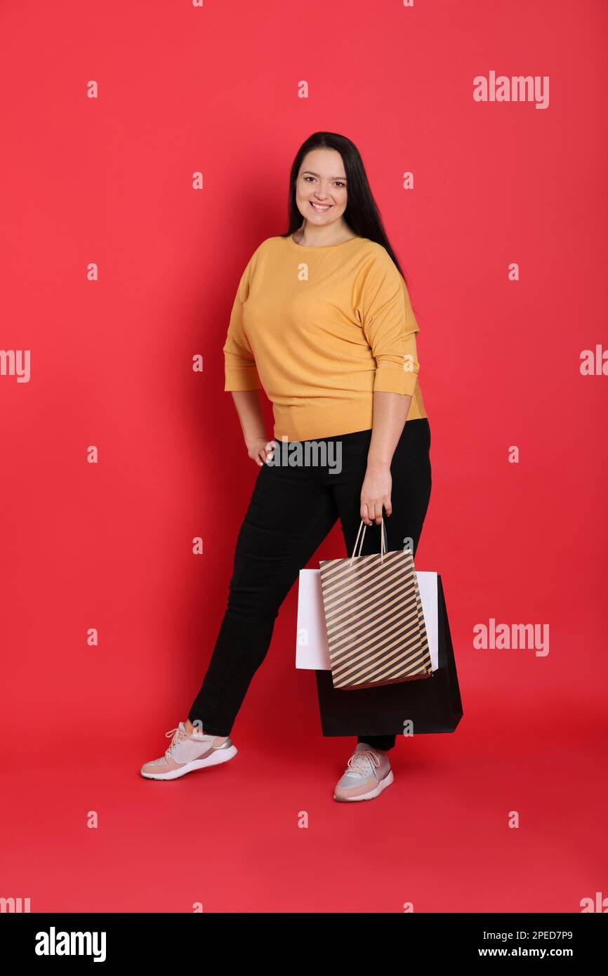 Beautiful overweight woman with shopping bags on red background Stock
