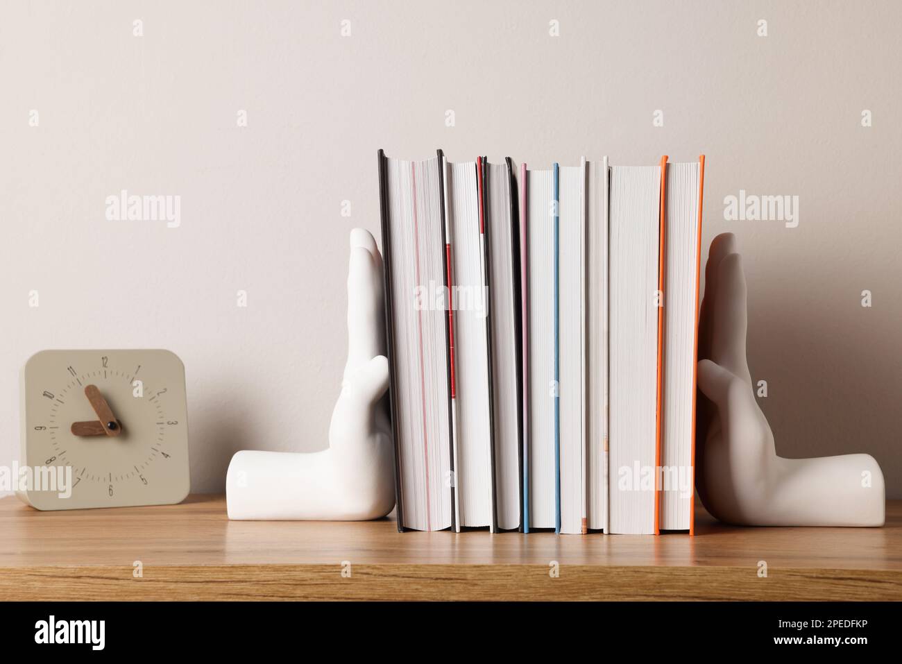 Beautiful hand shaped bookends with books and clock on table near light