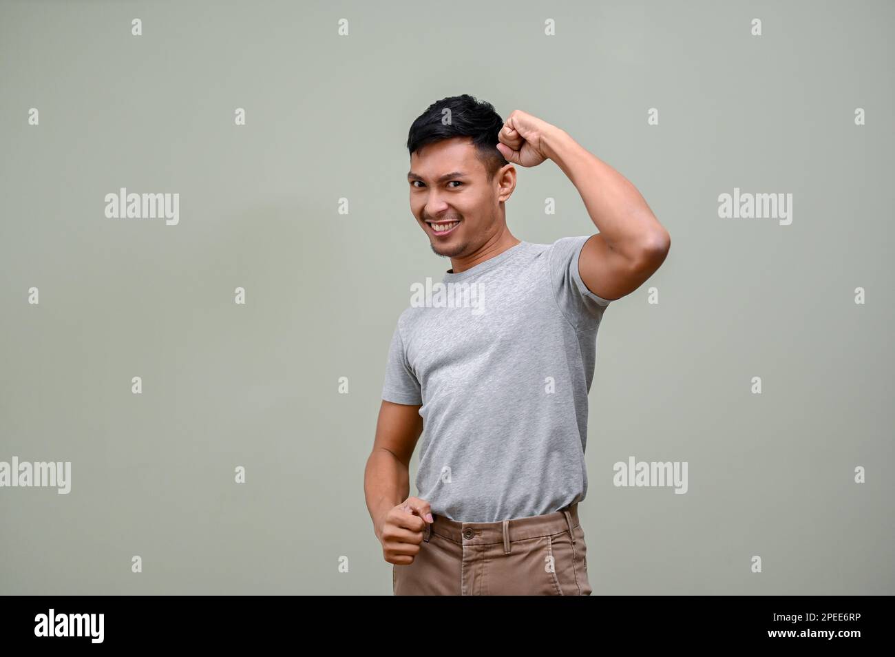 Happy millennial Asian man raising hand up, rejoicing, yes gesture, winning, victory, celebrating, archive goal. isolated green background Stock Photo