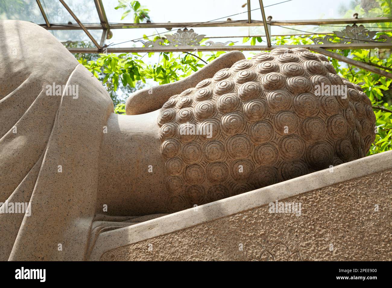 Big lying Buddha sculpture seen from behind in an Asian Buddhist pagoda. Giant reclining Buddha statue carved from stone, head back with hair snails Stock Photo