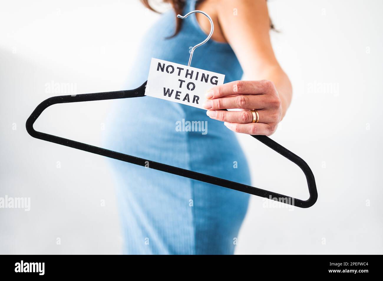 Nothing to Wear sign held by pregnant woman in the last month of pregnancy wearing stretchy blue dress showing her bump, maternity wear and inclusive Stock Photo