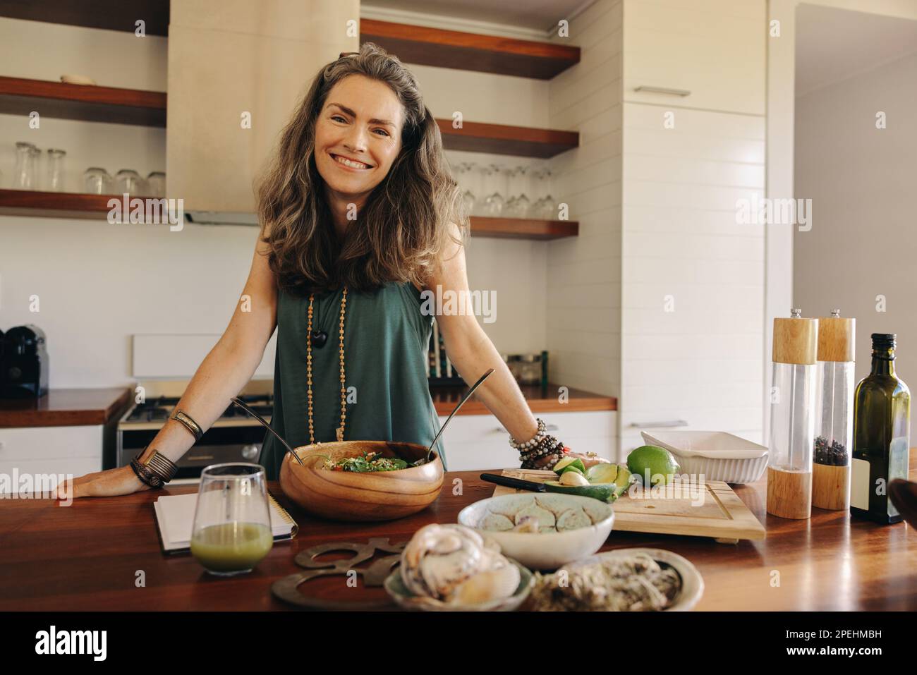Healthy senior woman smiling at the camera while preparing a vegetarian meal. Happy woman following a healthy plant-based recipe in her kitchen. Matur Stock Photo