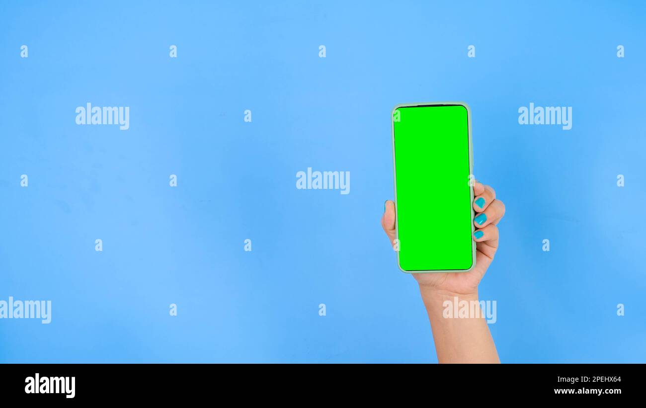 Female hand holding smartphone with mockup green screen on blue ...
