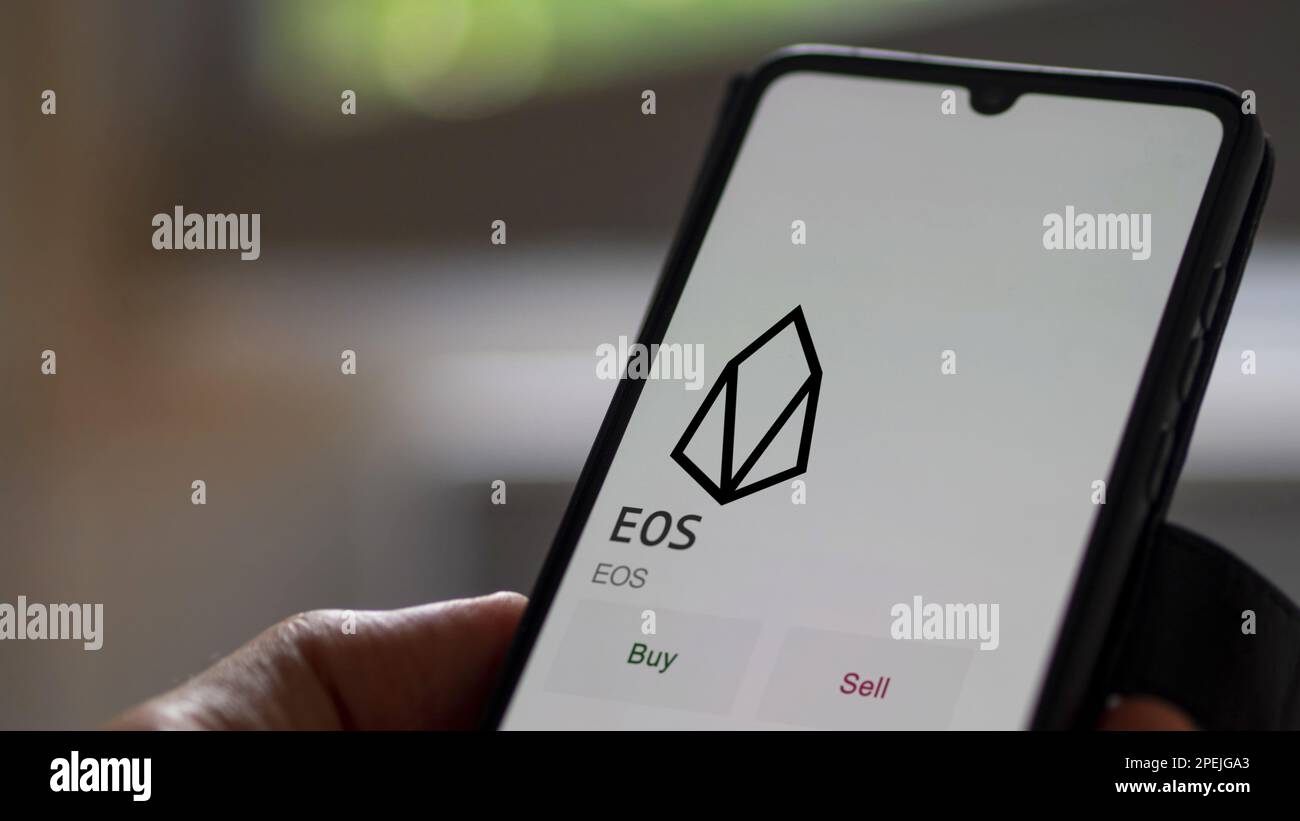 An investor analyzing the coin on screen. A phone shows the crypto's prices to invest in EOS blockchain assets. Stock Photo