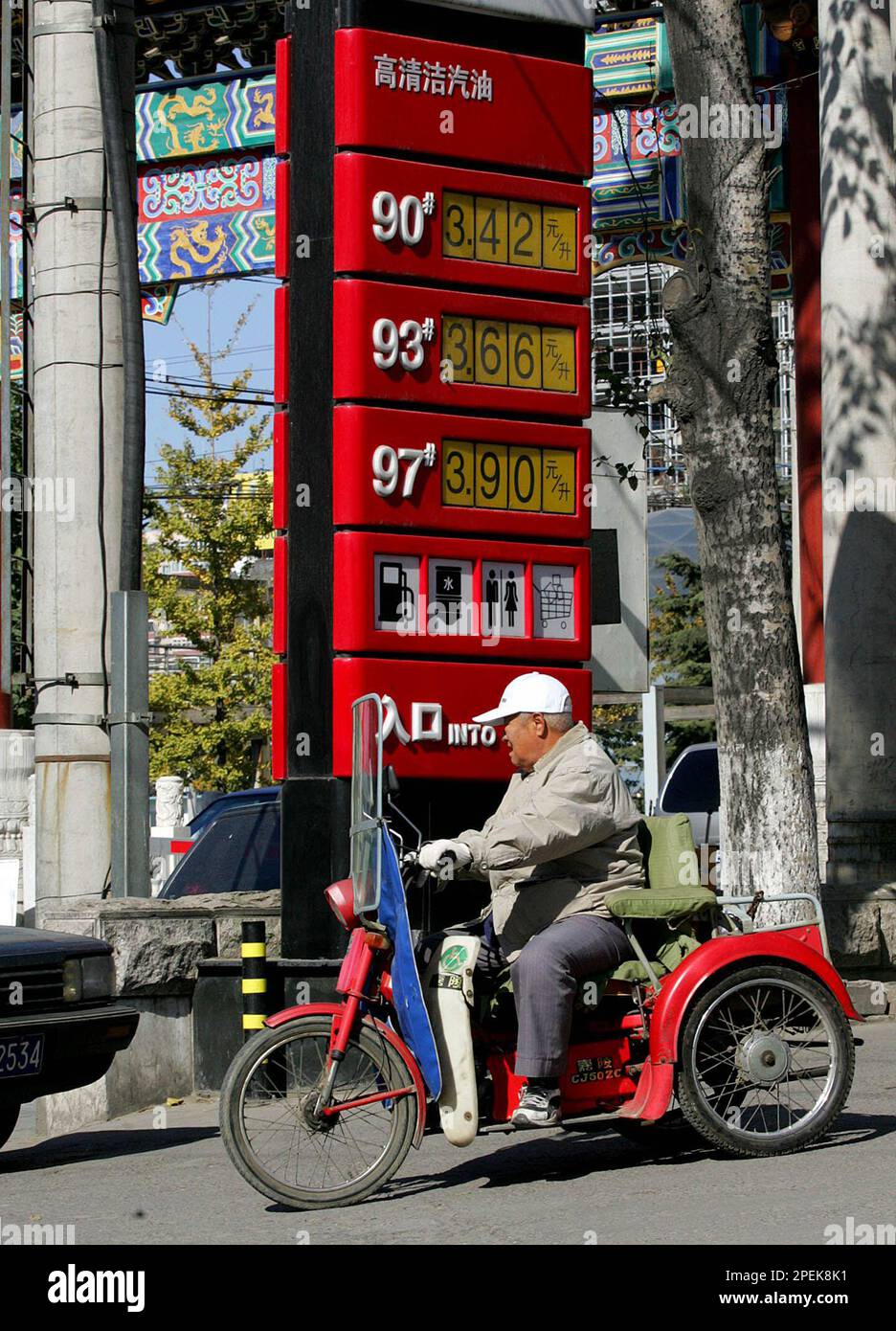 A man rides his motorized tricycle past a gas station sign showing