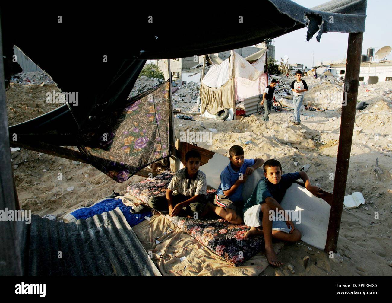 Palestinian youths sit in a makeshift tent at the site of their ...