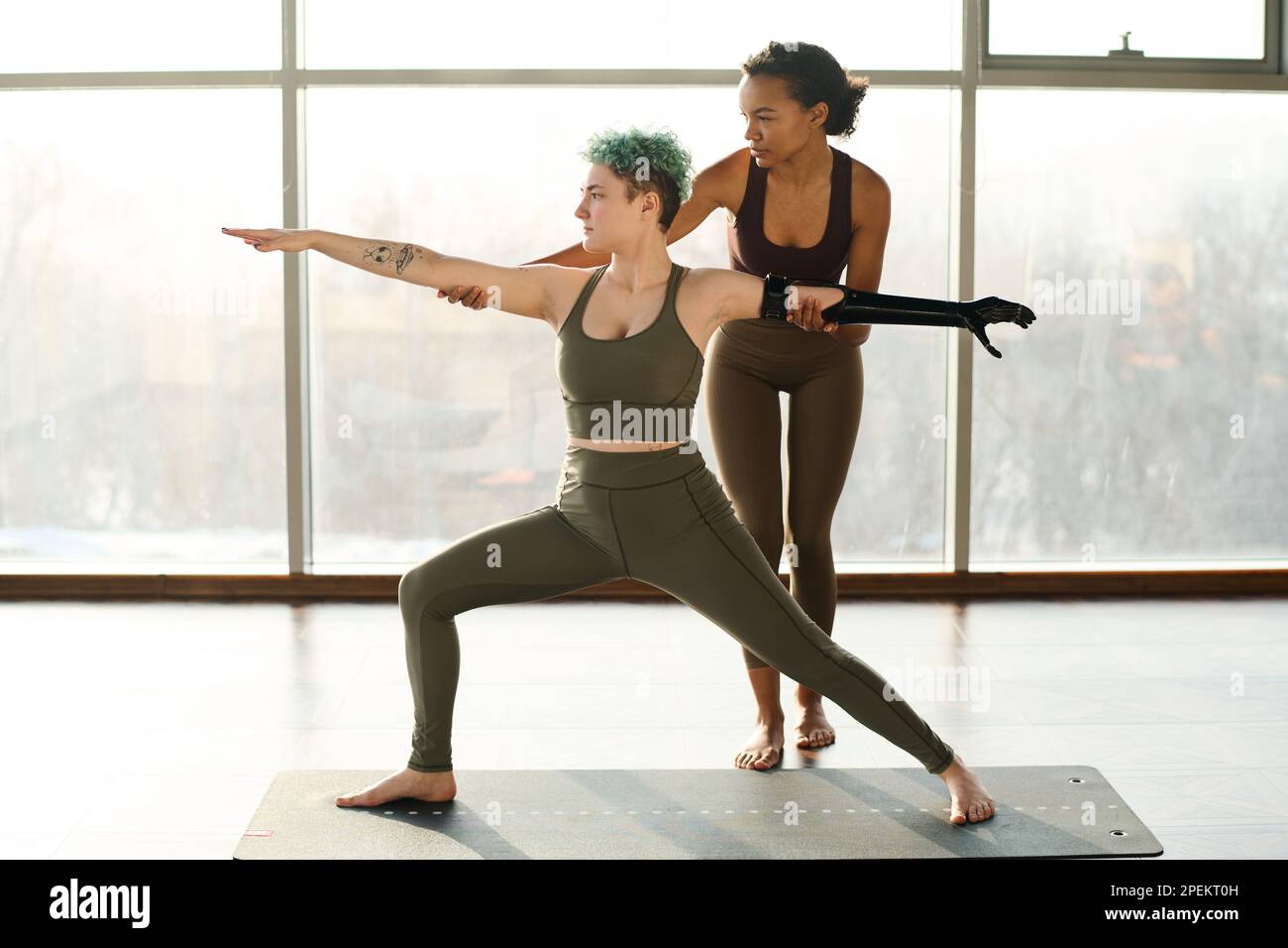 Young woman with prosthetic arm doing stretching exercises with instructor helping her Stock Photo