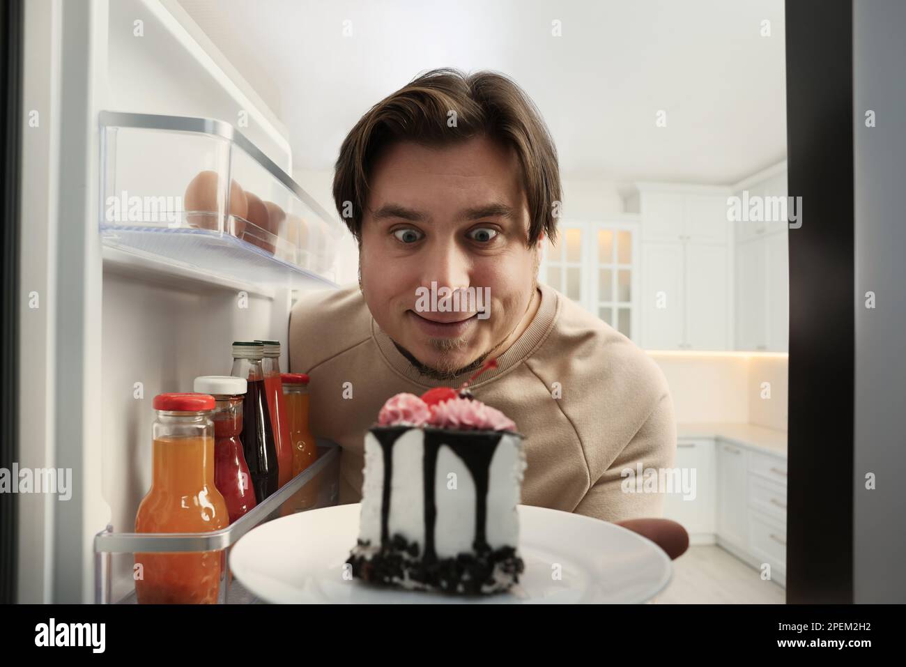 Happy overweight man taking cake out of refrigerator in kitchen, view