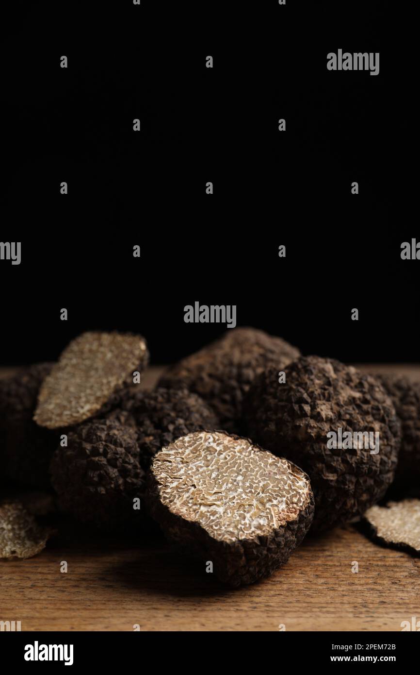 Whole and cut truffles on wooden table against black background Stock Photo