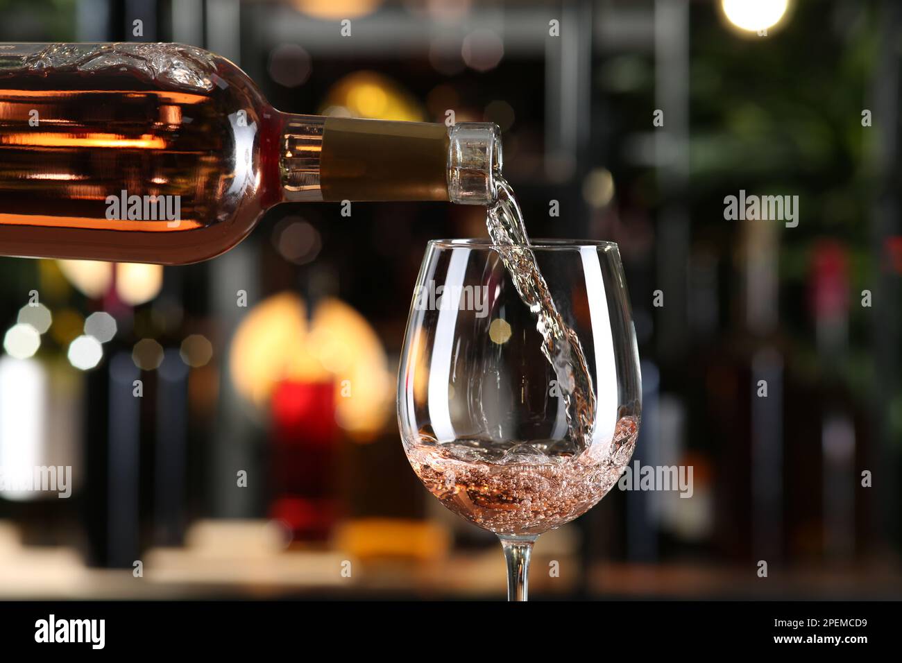 Pouring rose wine from bottle into glass on blurred background, closeup ...