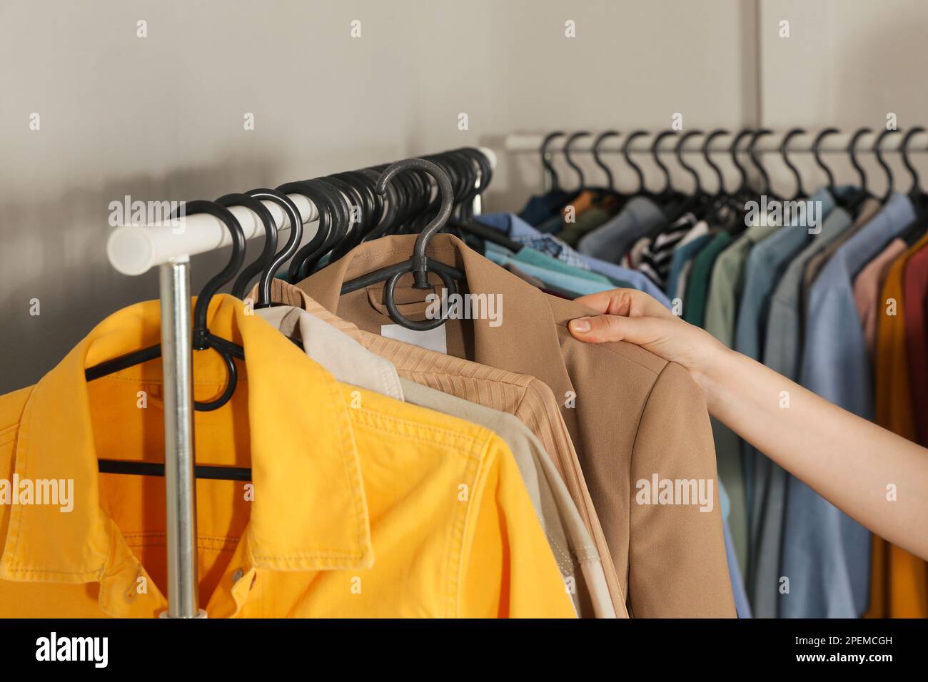 Woman picking clothes from rack indoors, closeup. Fast fashion Stock
