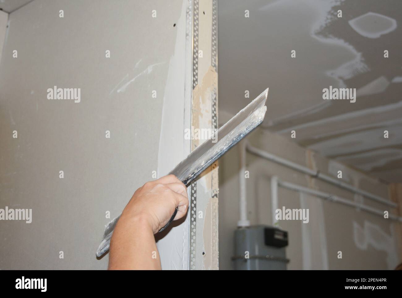 Builder plastering, skim coating, finishing, applying the first coat of plaster on a drywall partition wall  during house renovation. Stock Photo