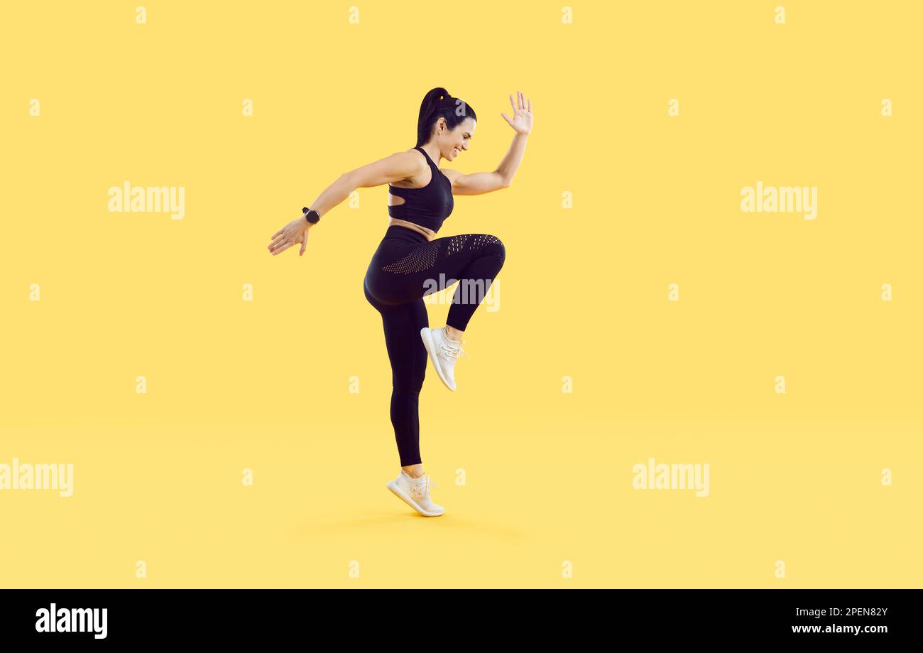 Active sporty woman doing high knees exercise isolated on vivid yellow ...