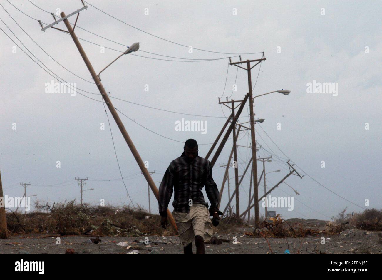 A Jamaican man walks as electrical poles are seen collapsed after the