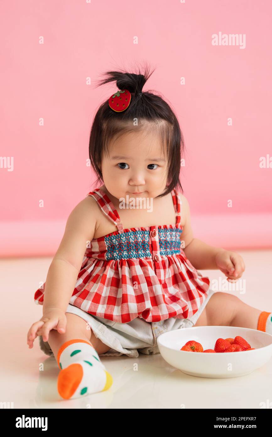 The lovely baby girls sit to eat strawberry Stock Photo