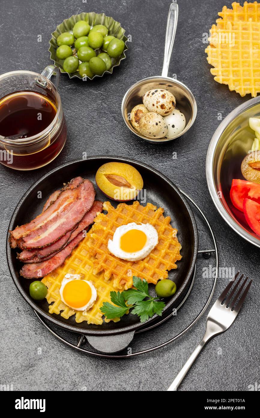 Waffles, fried bacon and eggs in a frying pan. A cup of tea, green