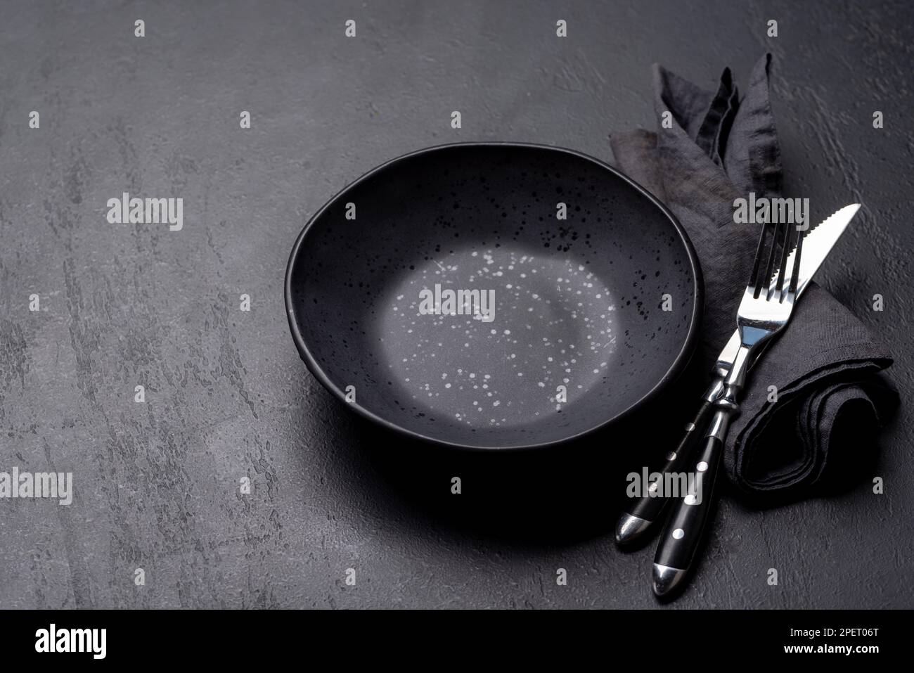 Empty plate with fork and knife on dark stone table. With copy space Stock Photo