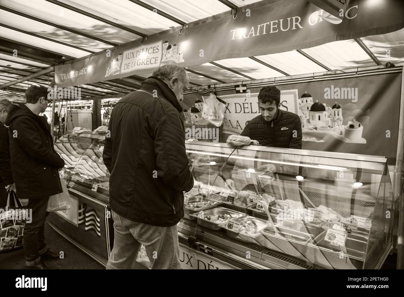 Saint-Maur-des-Fosses, France - October 8, 2022: People buy freshly prepared traditional dishes from Greek deli stall at a street market. Sepia photo. Stock Photo