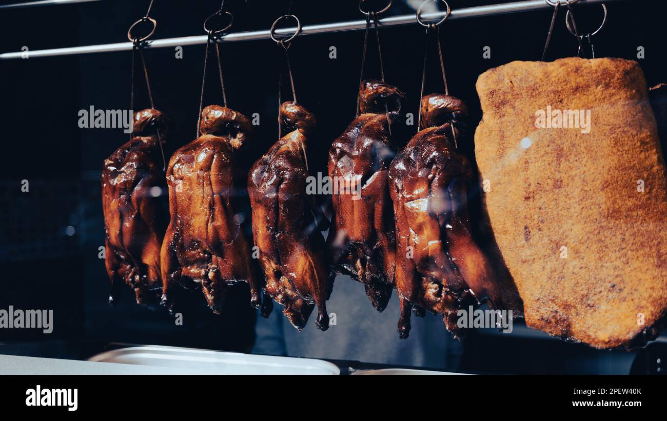 Roasted crispy ducks hanging from metal meat hooks in the window of a