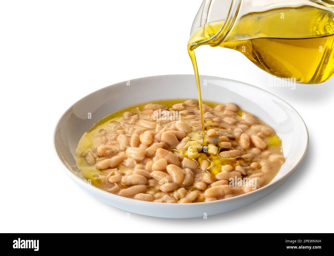 Extra virgin olive oil pouring from glass jug over bean soup in white dish isolated on white with clipping path included Stock Photo