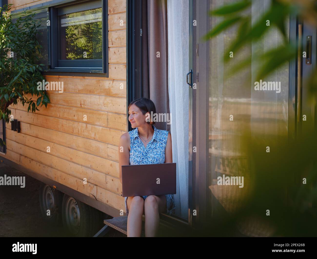 Happy young asian woman with laptop resting outdoors near tiny house