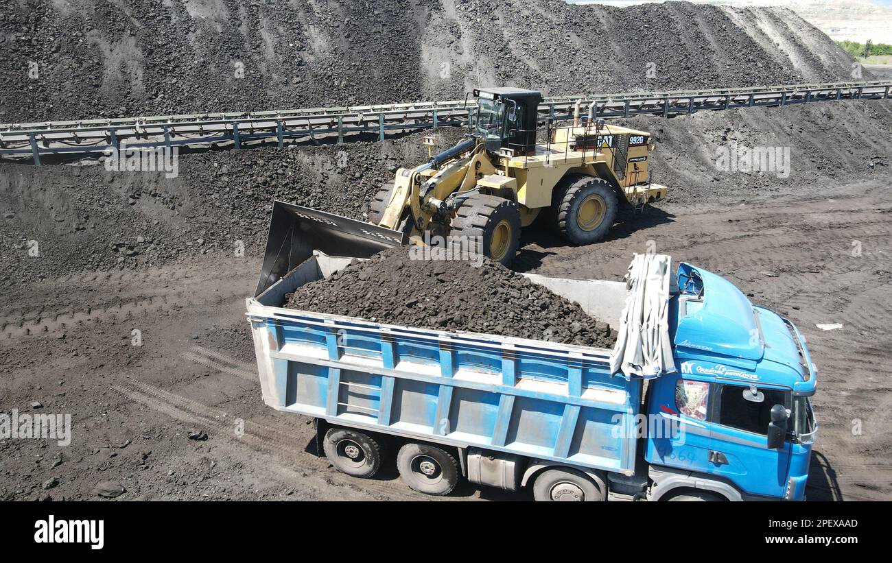 Wheel Loader loading coal on trucks, working at a huge mining site. Stock Photo