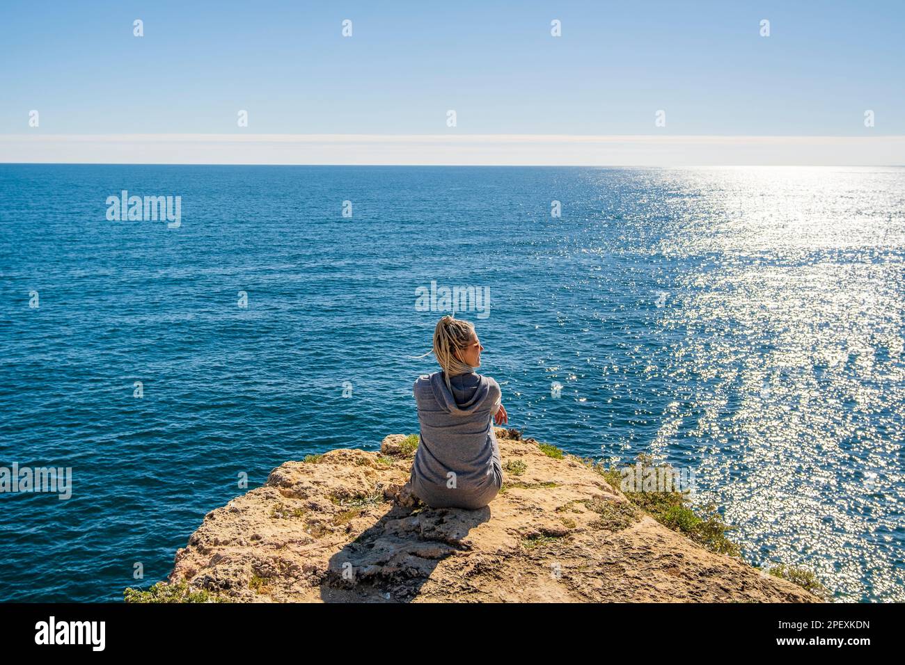Back of young woman sitting on the top of cliffs immersed in the beauty ...