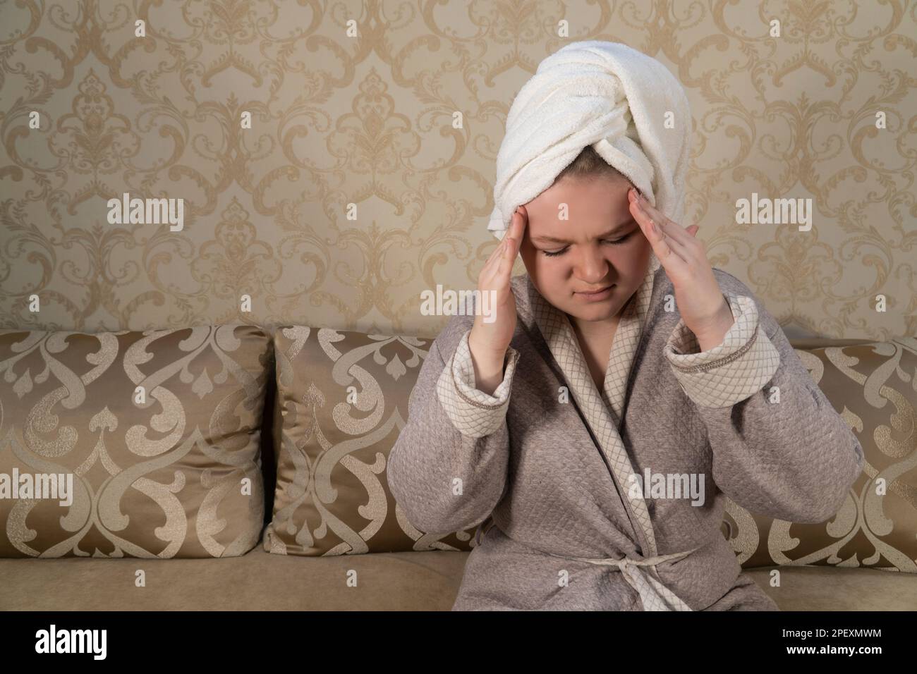 Girl in the room is sitting on the couch, holding her head in her hands. Headache. The concept of medicine, pharmacy, healthcare and home treatment Stock Photo