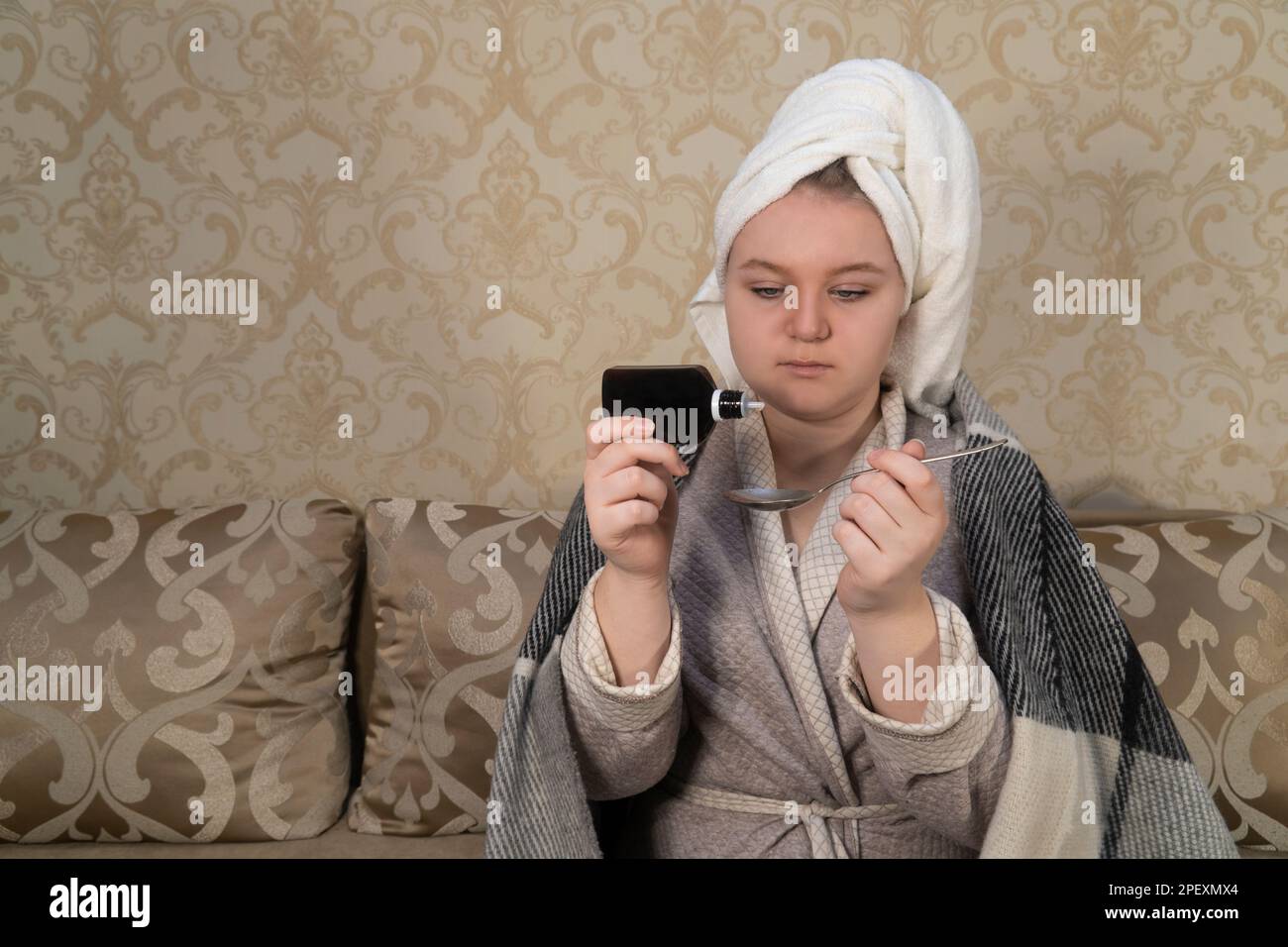 A girl in a plaid sits on a sofa and drips medicine from a bottle into a spoon. Concept of medicine, healthcare, pharmacy and home treatment Stock Photo