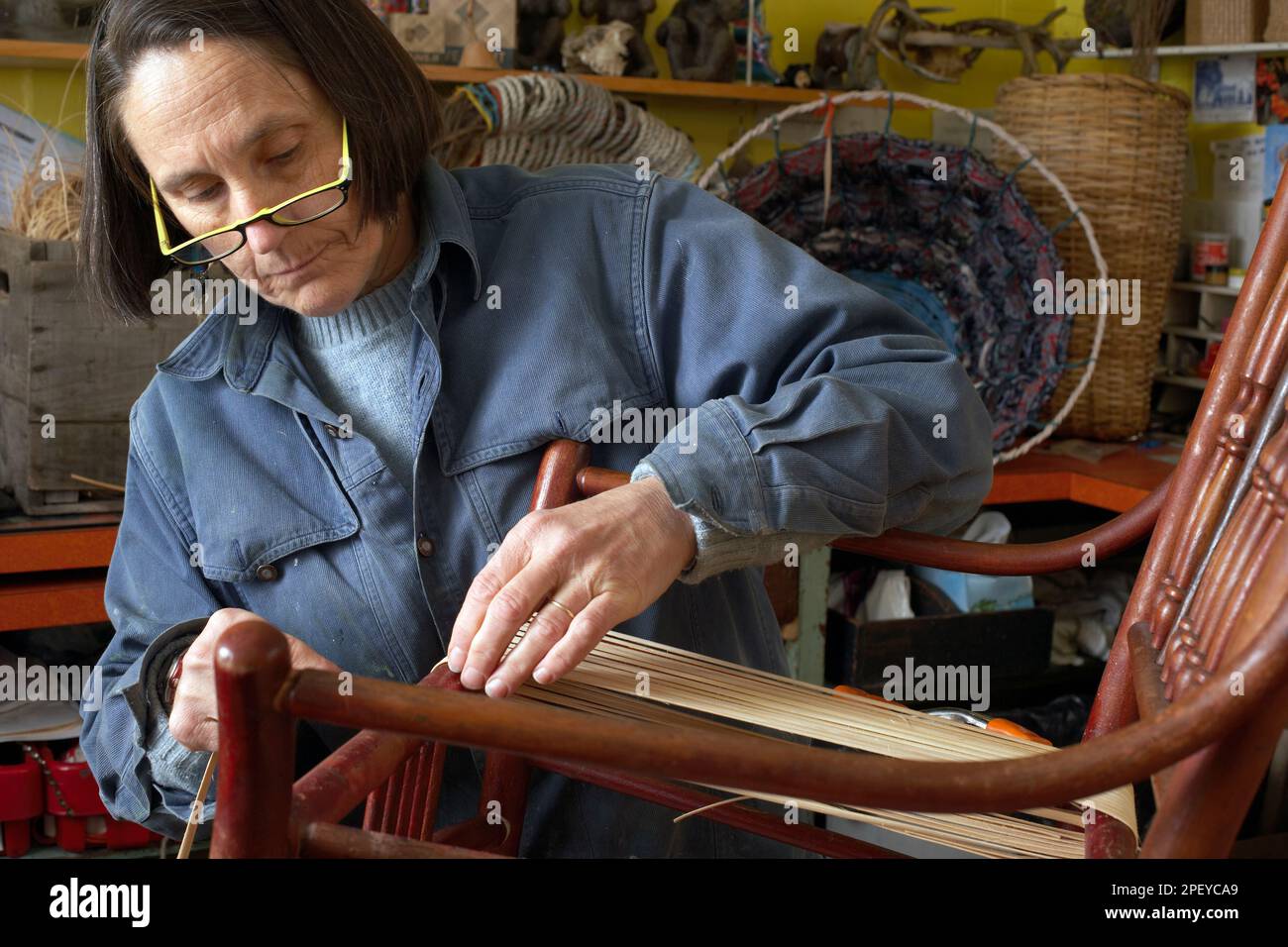 Female artisan weaves new caning onto an antique rocking chair Stock Photo