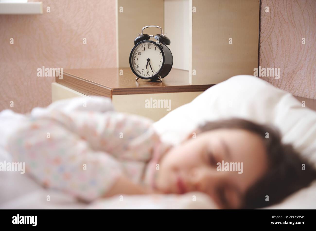 Focus on black alarm clock showing half past six, on bedside nightstand
