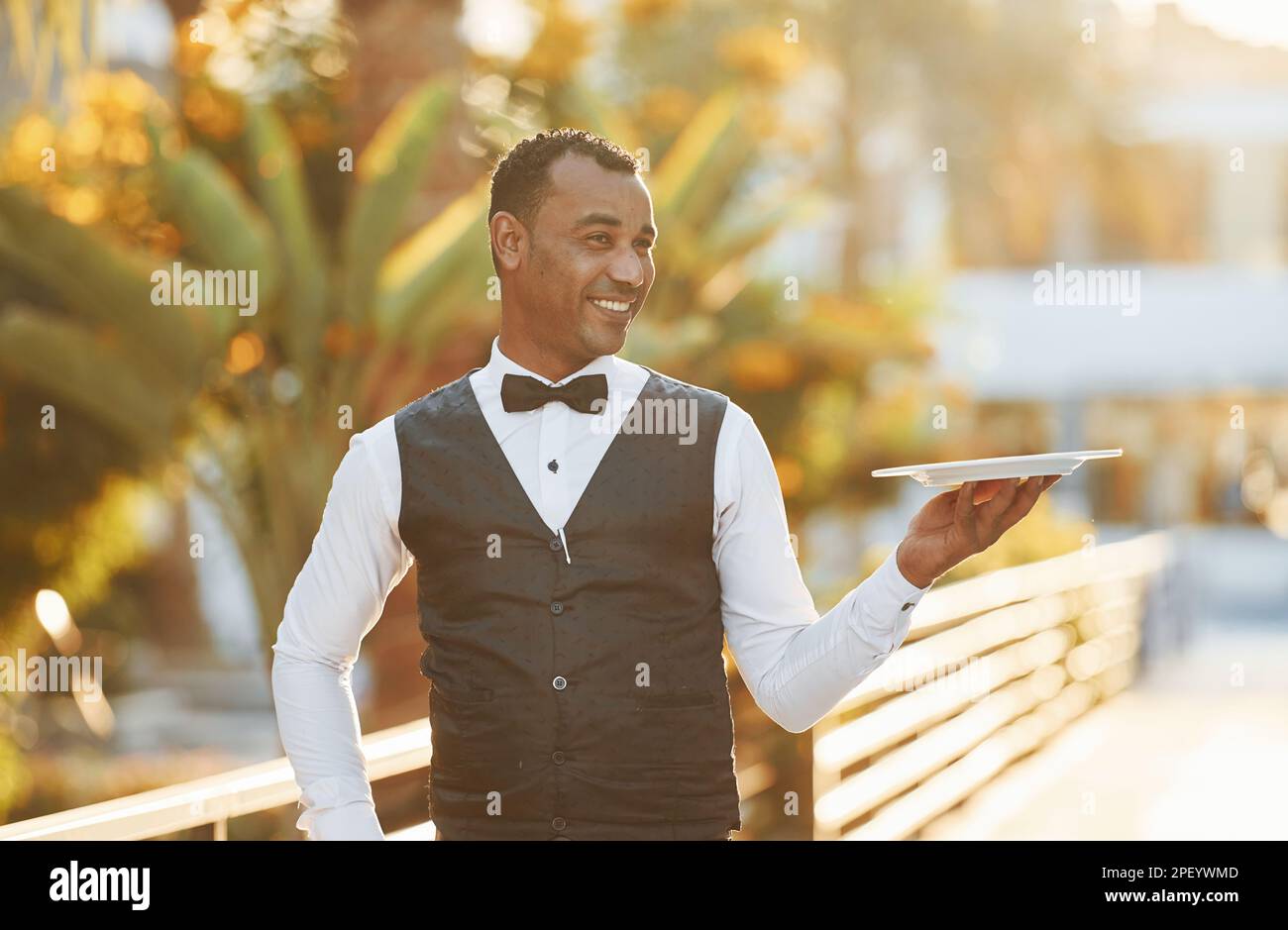Holds empty plate. Black waiter in formal clothes is at his work