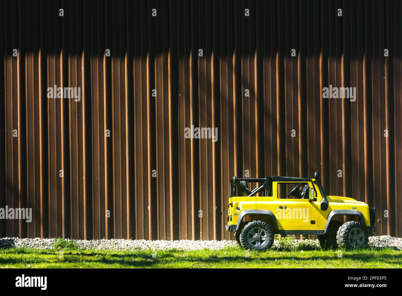 Childrens battery powered yellow vehicle parked beside of brown tin building on a sunny day in Dorothy, WV USA Stock Photo