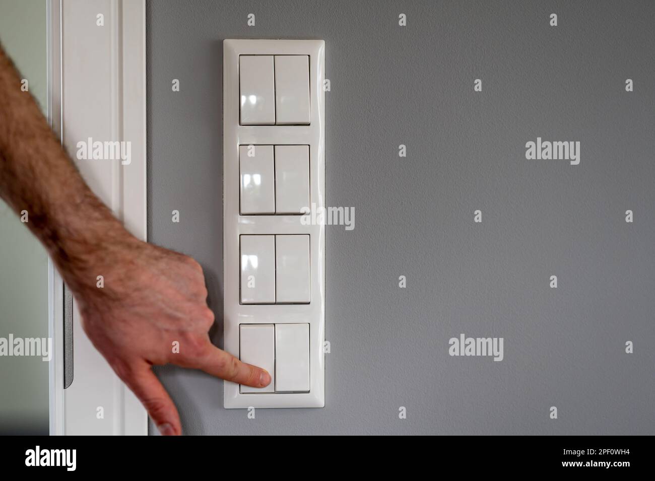 Row of eight light switches, while a finger switches on one light switch. Stock Photo