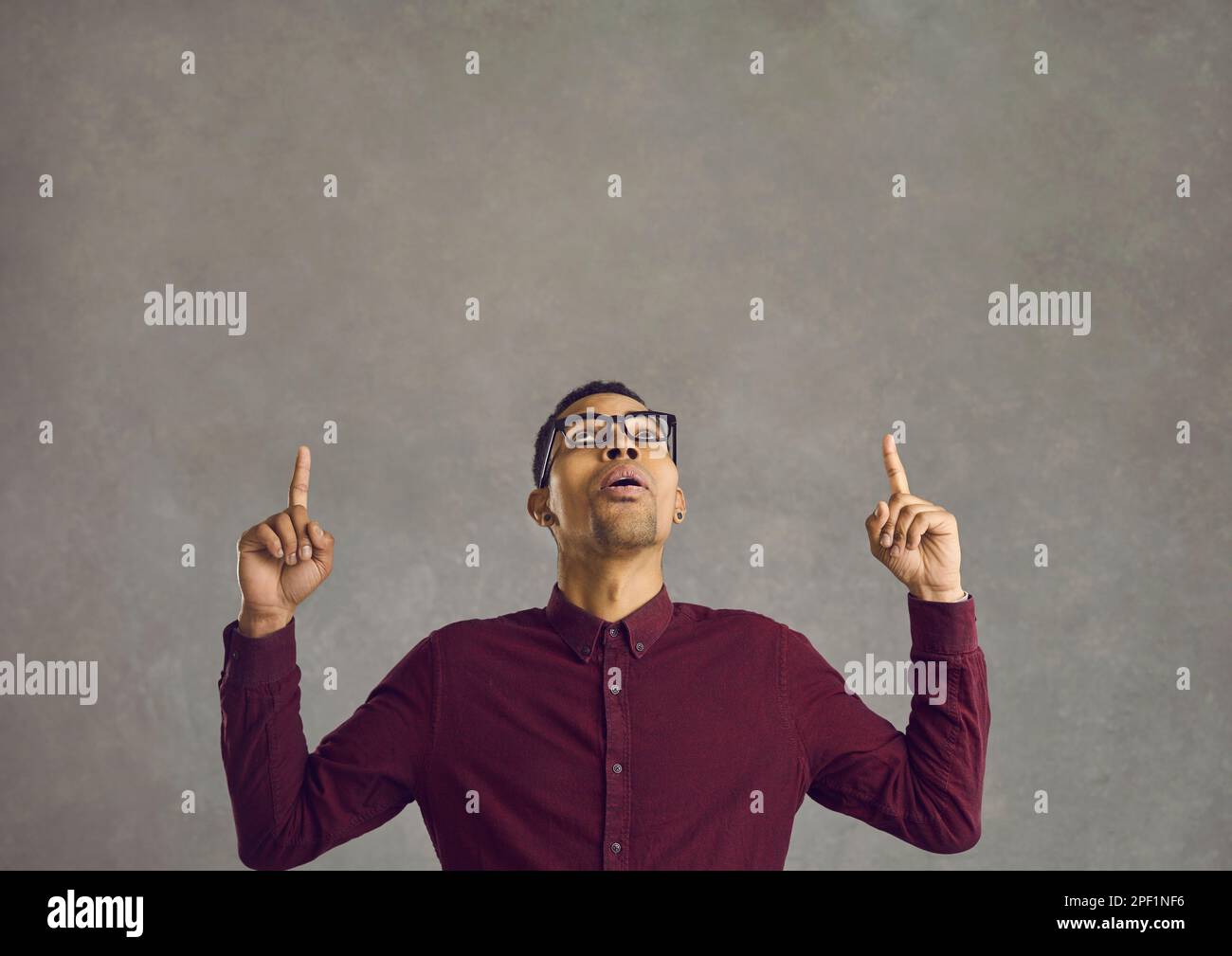 Surprised young black man pointing with both fingers at something on copy space above Stock Photo