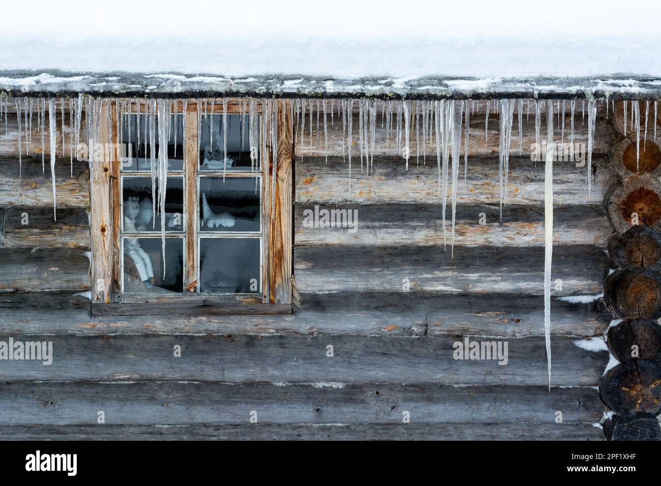 Rectangular window on a log wall and large icicles hanging from the eaves. From the Window of the World series. Stock Photo