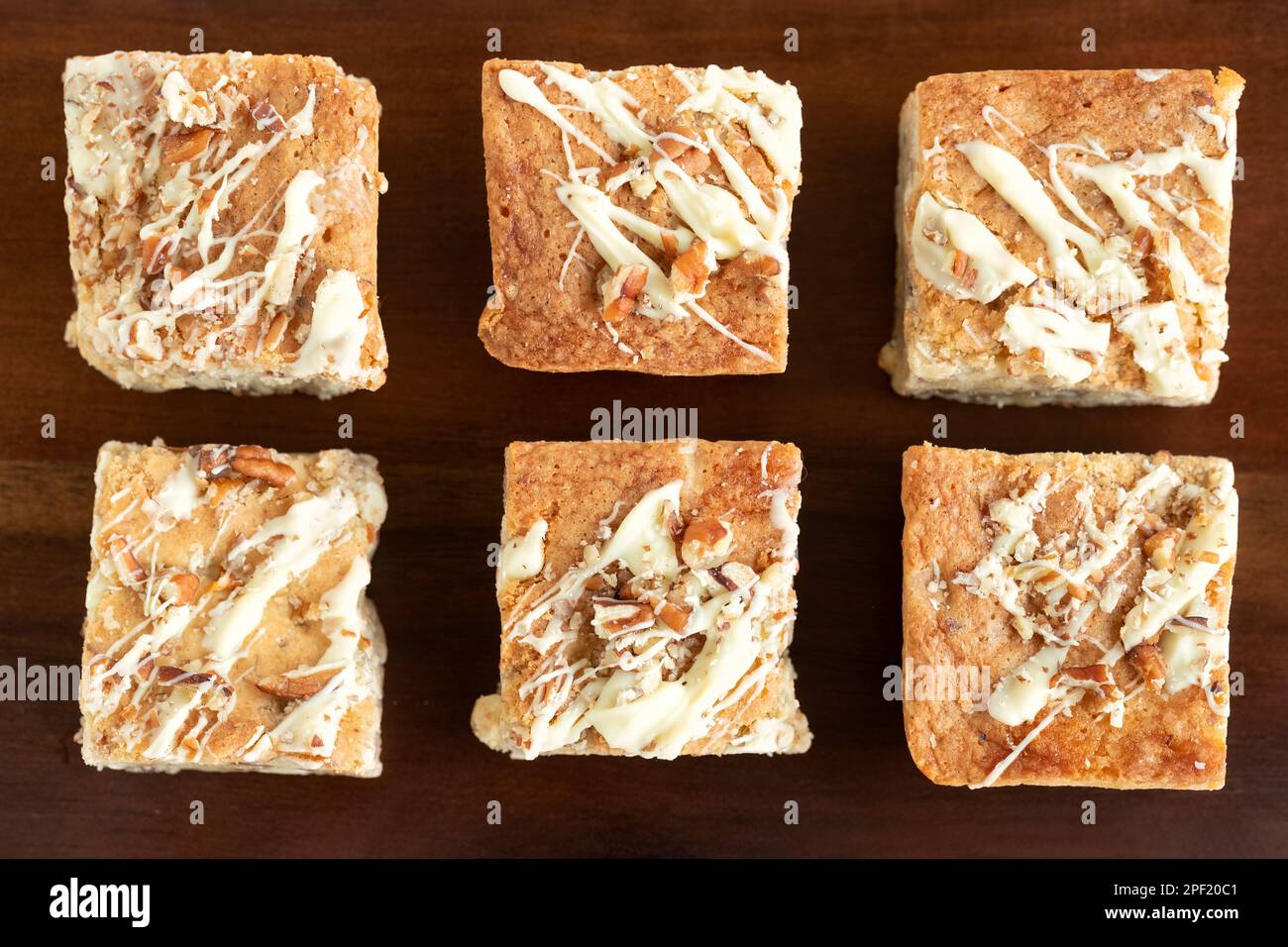 A overhead view of home baked white chocolate pecan Blondies arranged on a wooden platter. The blondies are still warm and gooey. an indulgent treat Stock Photo