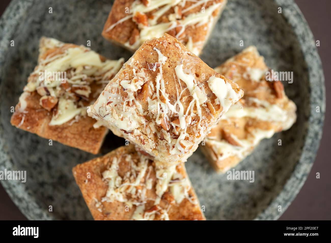 A overhead view of home baked white chocolate pecan Blondies arranged on a marbled plate. The blondies are still warm and gooey. an indulgent treat Stock Photo