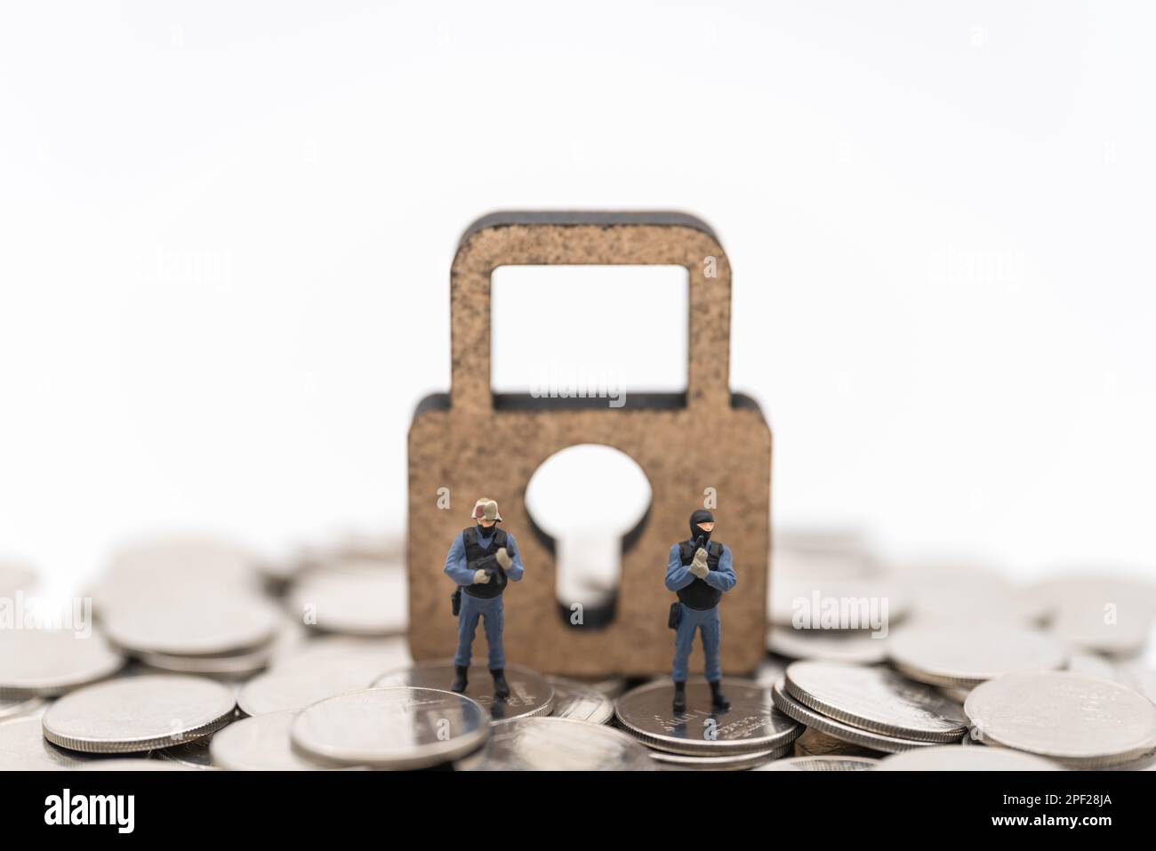 Money and Security Concept. Two soldier /police guard miniature figures people standing on pile of coins with wooden master key lock icon on white bac Stock Photo